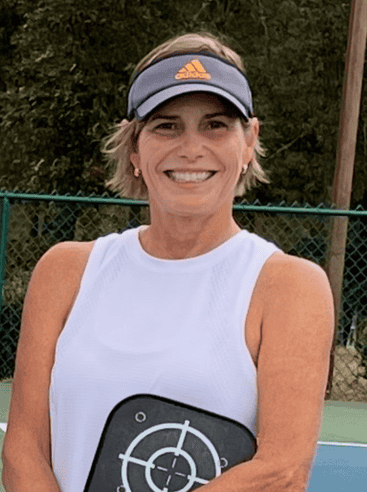 A travel highlight captured by Straight Away Travel shows a smiling woman posing on an outdoor pickleball court with a beautiful tropical mountain backdrop. She is wearing a sleeveless white athletic top, a patterned black and white tennis skirt, a white visor, and sunglasses while holding a blue pickleball paddle. Behind her, lush palm trees and green mountain peaks rise under a bright blue sky with soft white clouds.